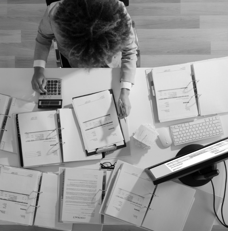 A desk of open contract binders and a calculator, worked through from above